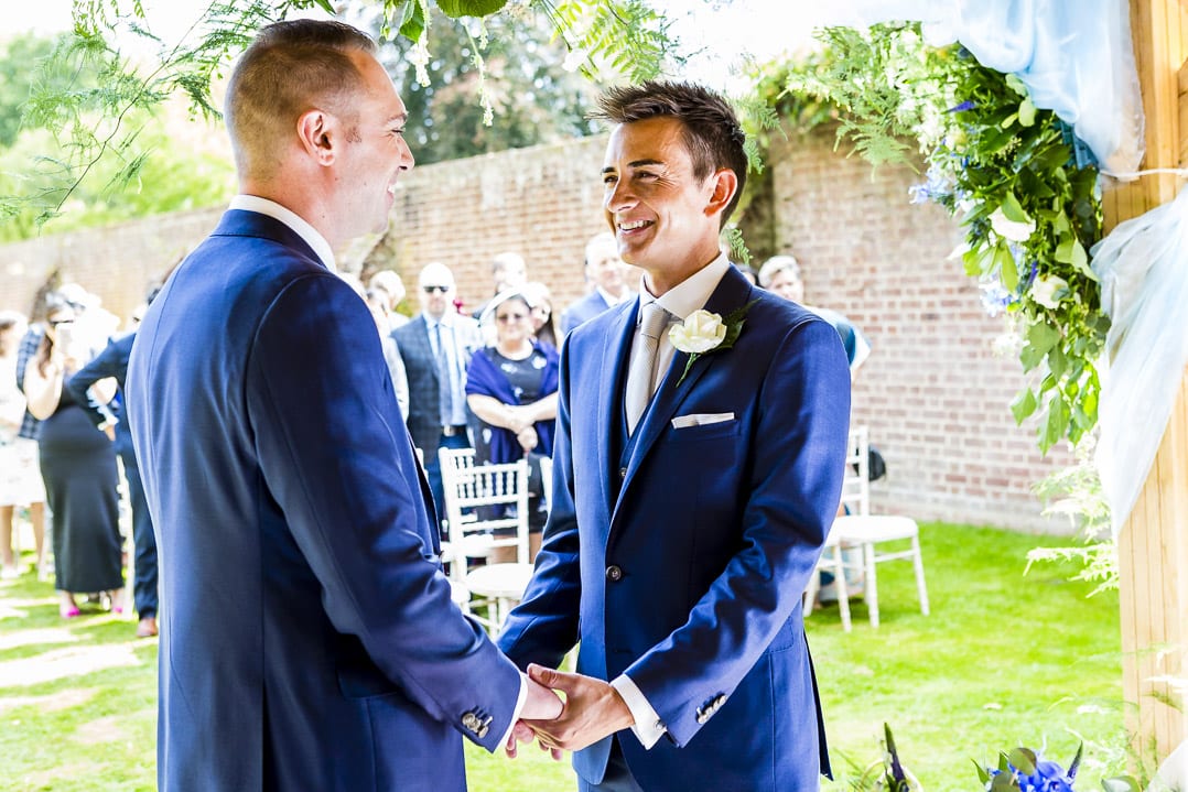 TWO GROOMS HOLDING HANDS DURING THEIR OUTDOOR WEDDING CEREMONY