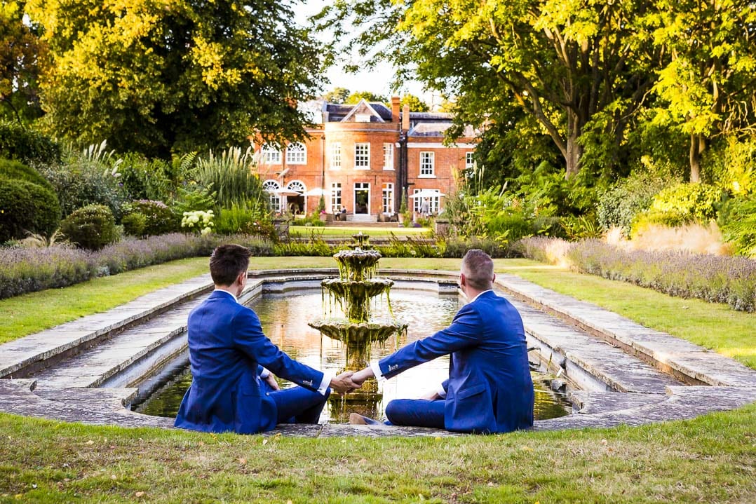 two groom hold hands by the pond and look out to Royal Berkshire Hotel