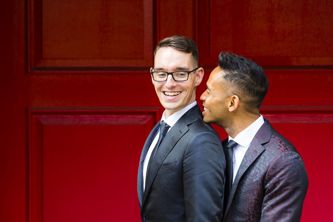 Two gay men embrace in front of a red door on their wedding day