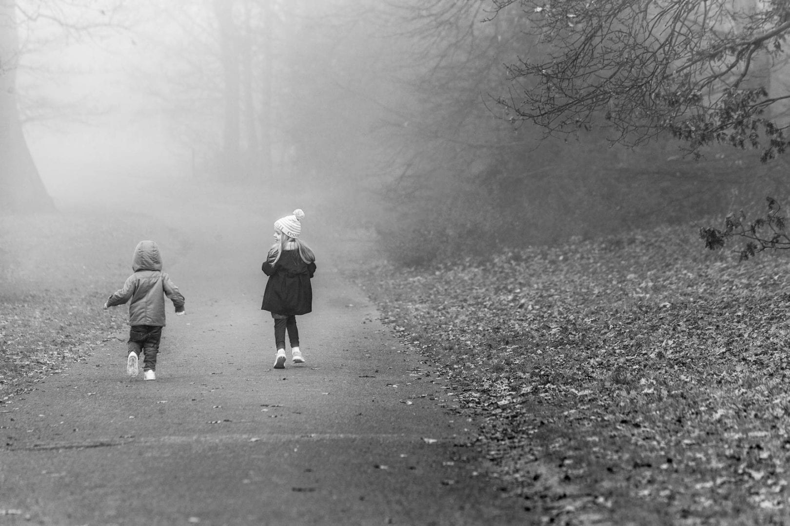 A young boy and girl run down the hill on a foggy day