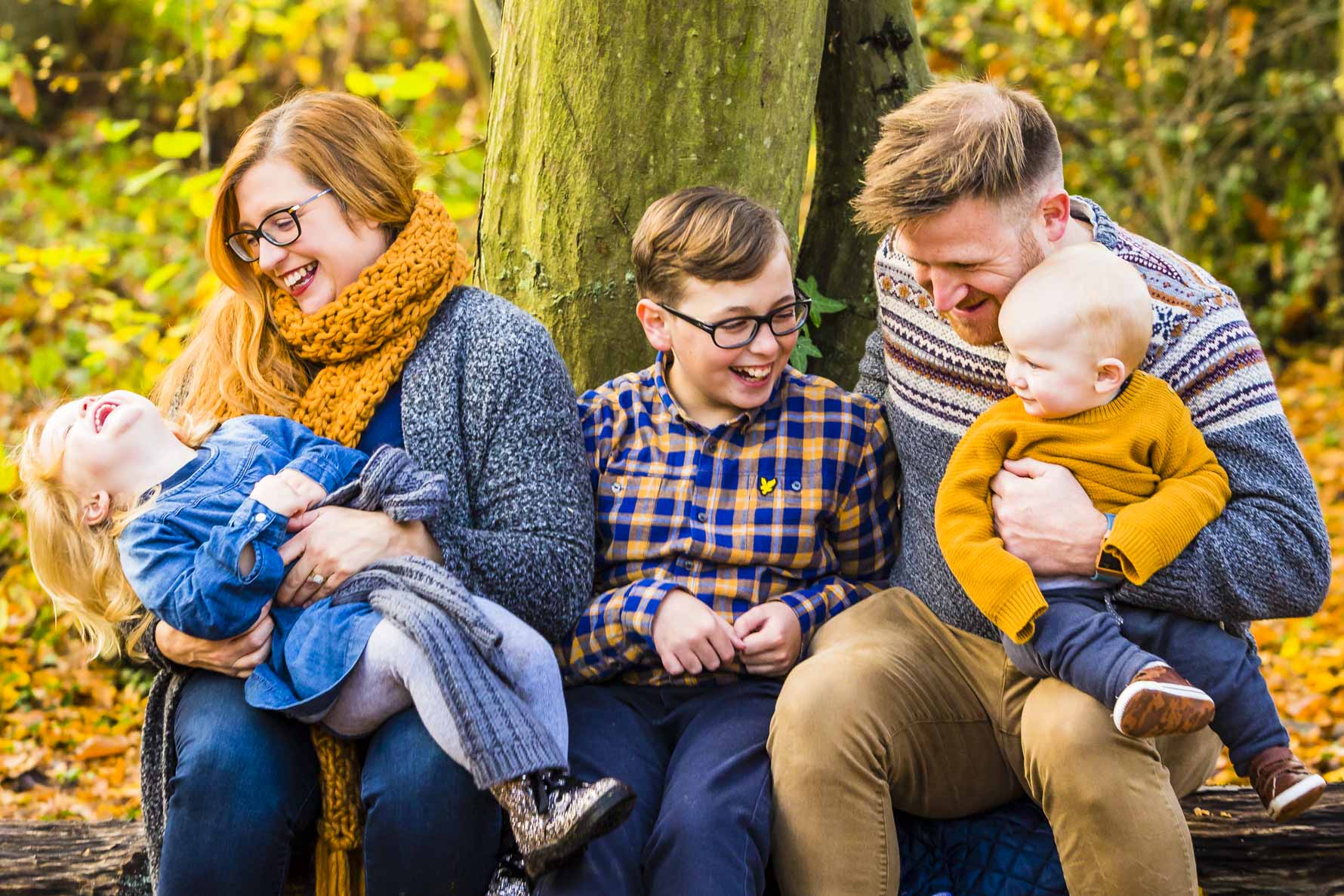 Two parents and three children laugh as they tickle one another in the autumn woodland
