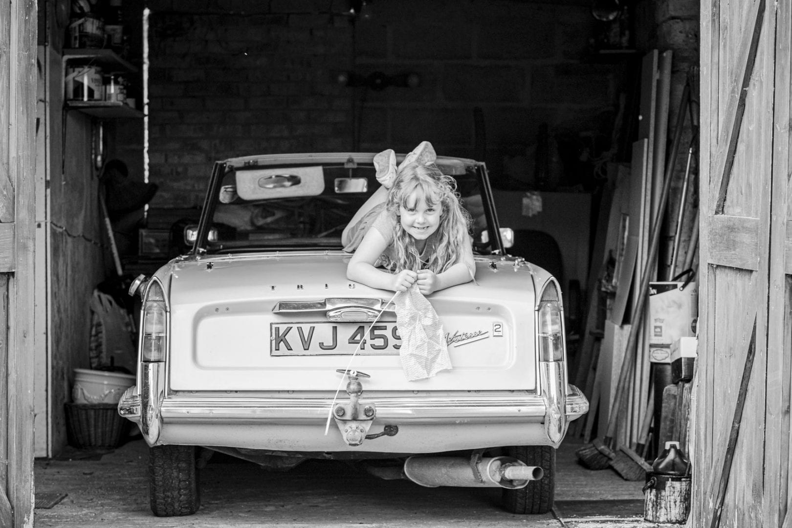 A young girl lies on the bonnet of a vintage car in the garage