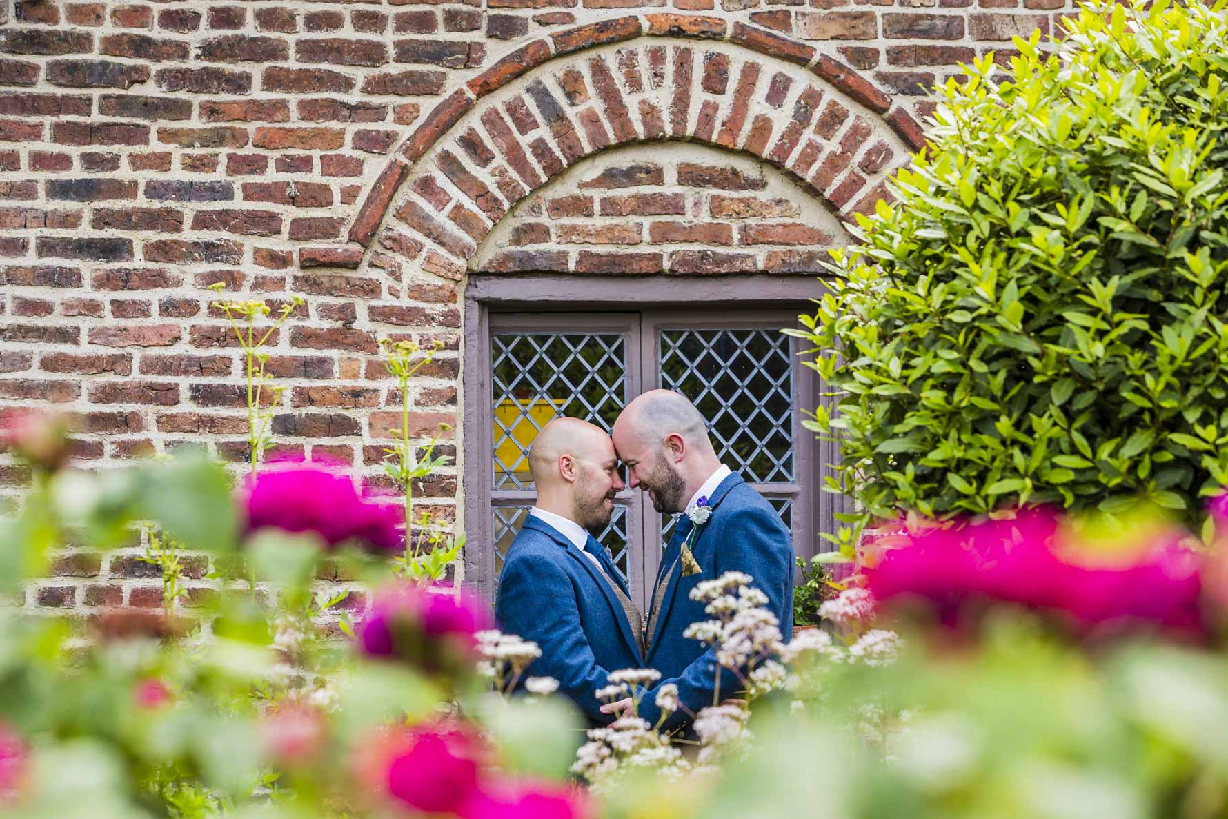 Two grooms with foreheads together in the garden fo their wedding venue. Gay wedding photography.