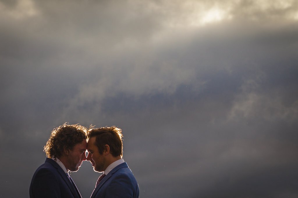 Two grooms pose under a cloudy sky