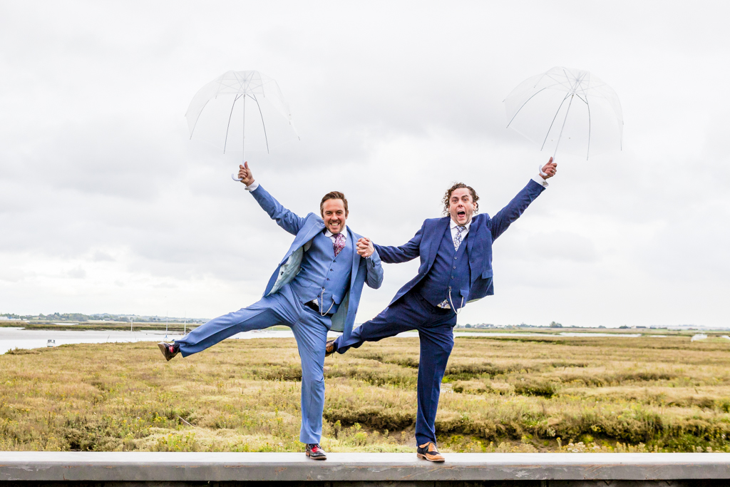 Two grooms pose with umbrellas