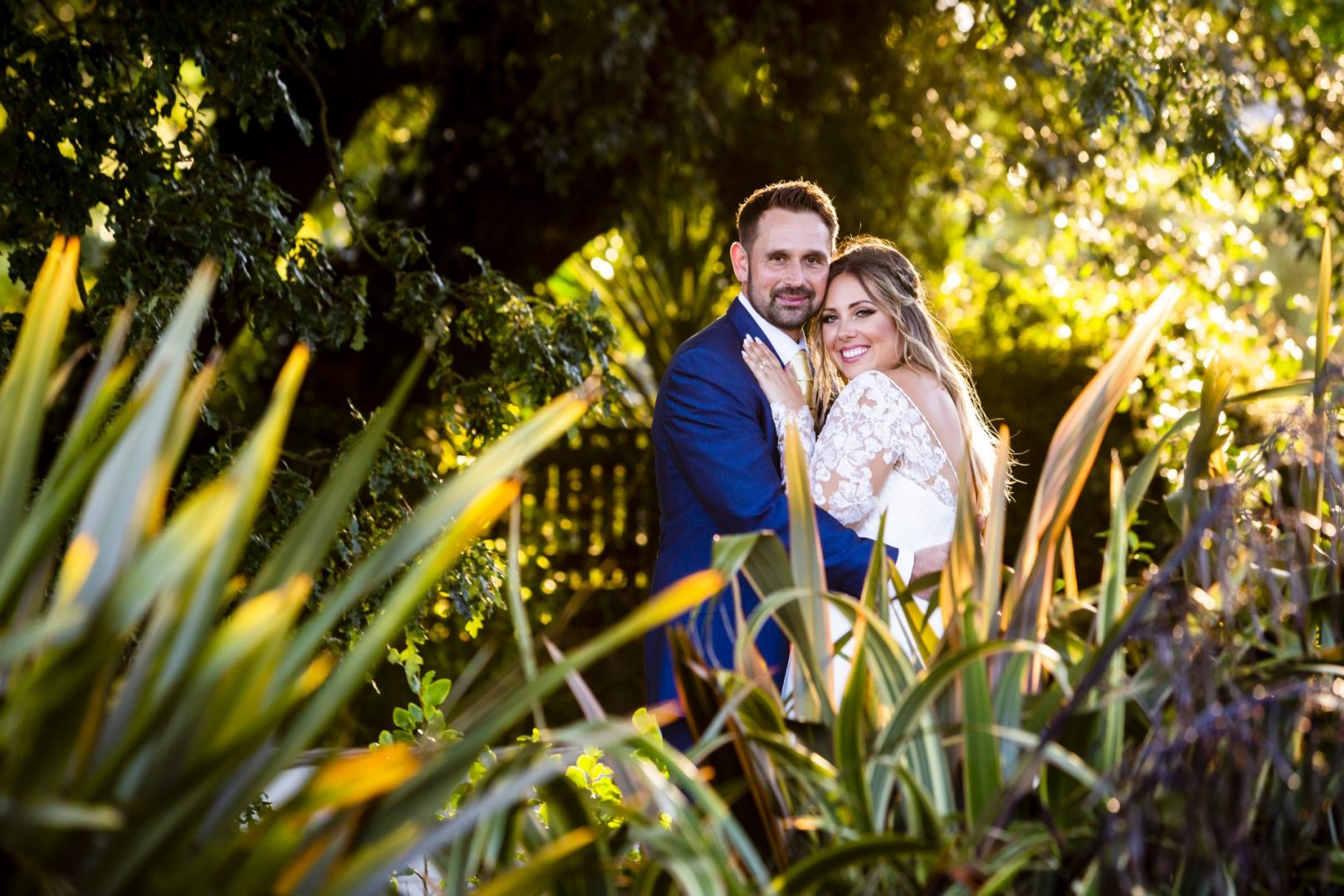 A bride and groom pose amongst sun-kissed foliage for Essex Wedding Photographer Ross Will