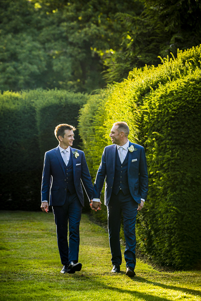 Two grooms hand in hand walking towards the camera