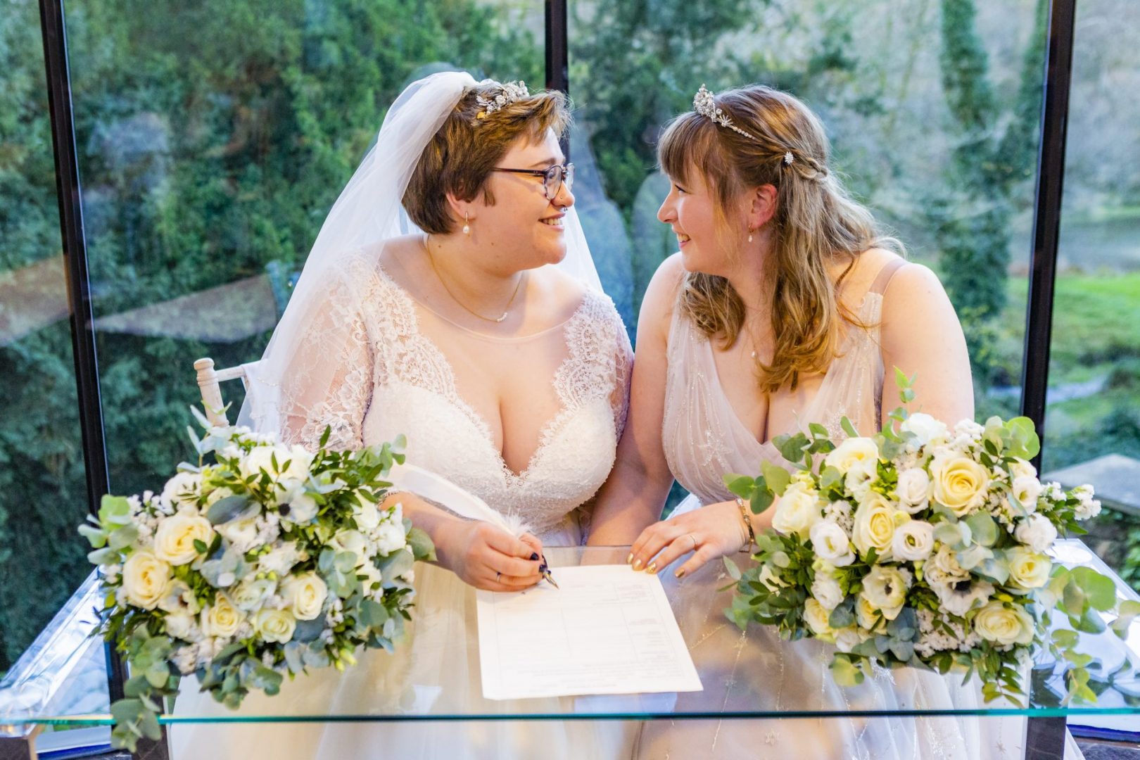Two brides smile at each other as they sign the register