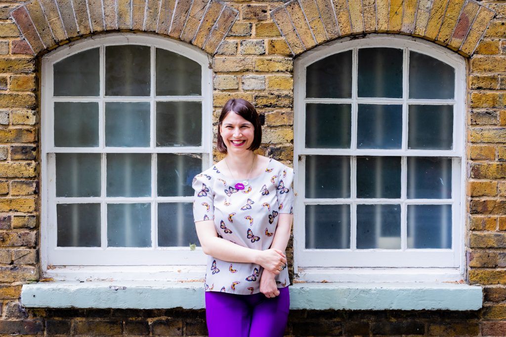 Kathryn Palmer-SKillings leaning against a brick wall between windows