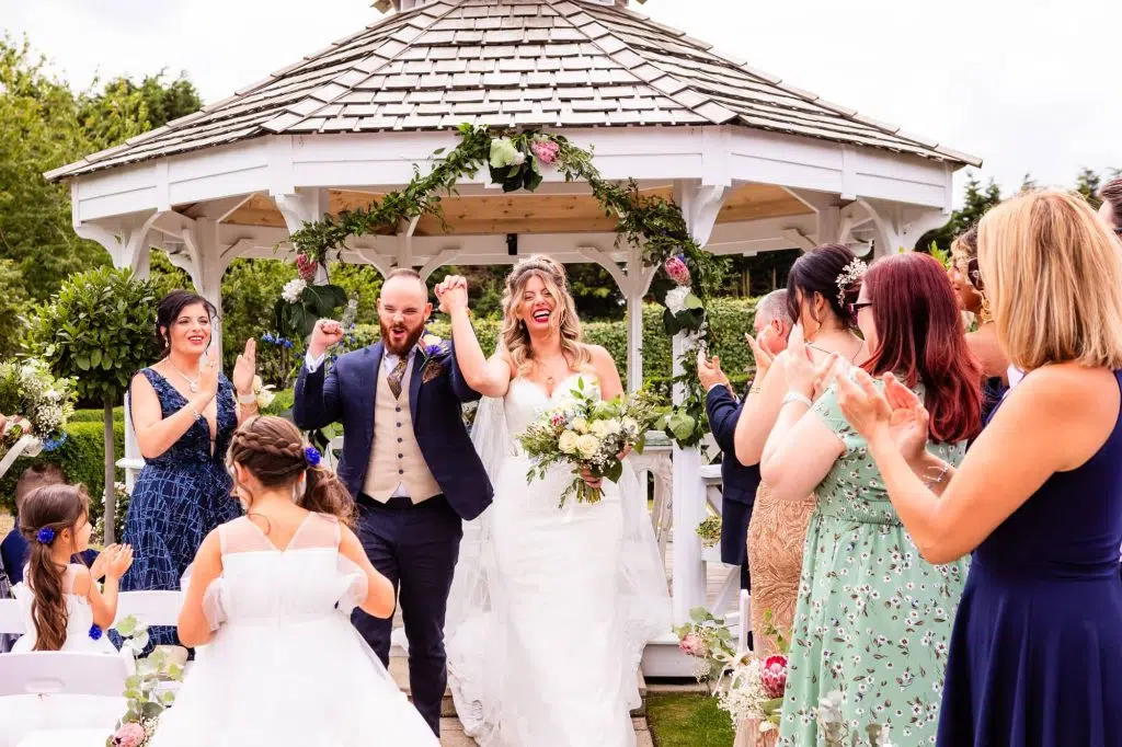 A bride and groom laugh as they exit their outdoor wedding ceremony at The Lawn, Essex