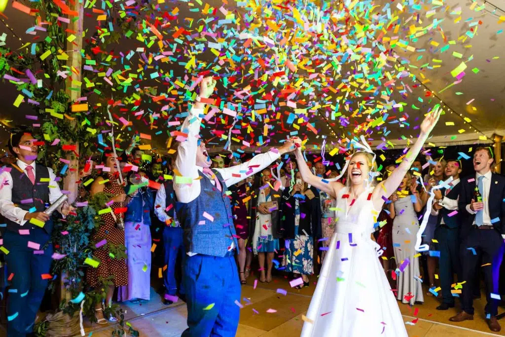 A newly married couple throw their hands up in the air as confetti rains down on them on their dance floor.