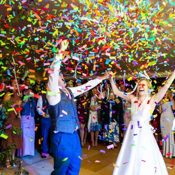 A newly married couple throw their hands up in the air as confetti rains down on them on their dance floor.