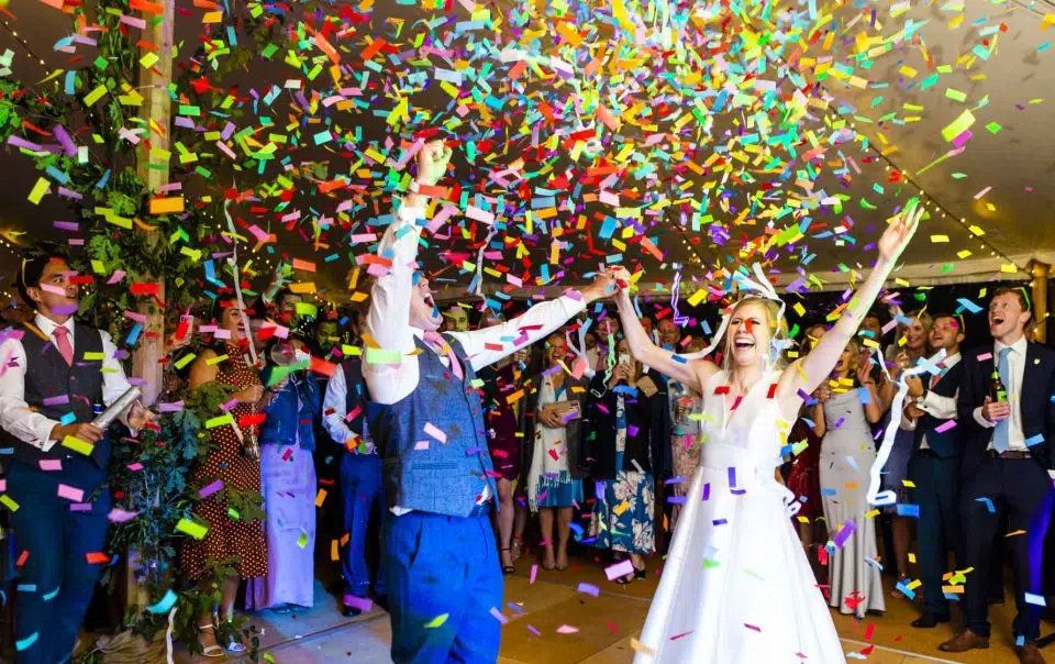 A newly married couple throw their hands up in the air as confetti rains down on them on their dance floor.