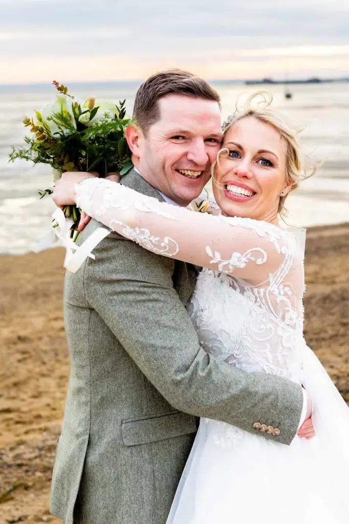 A couple pose on the beach after their Essex wedding
