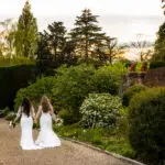 Two brides walking in the gardens of Gaynes Park, Essex. Captured by their gay wedding photographer.