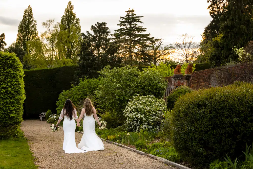 Two brides walking in the gardens of Gaynes Park, Essex. Captured by their gay wedding photographer.