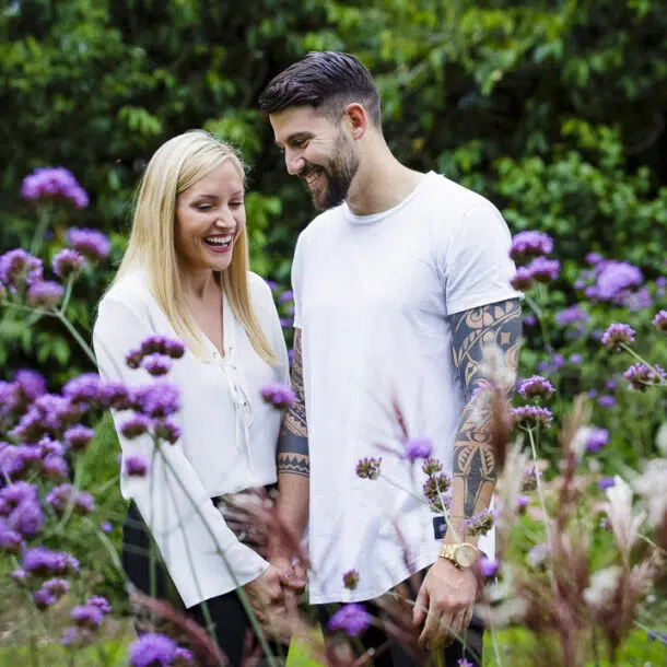 An engaged couple laughing amongst flowers on their engagement photoshoot