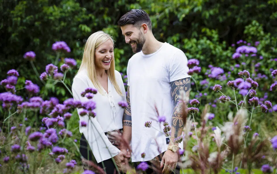 An engaged couple laughing amongst flowers on their engagement photoshoot