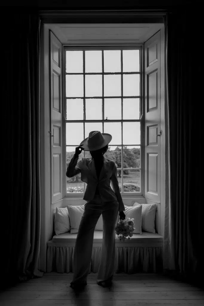 a bride sollhoutted against the large window in the bedroom at butley priory