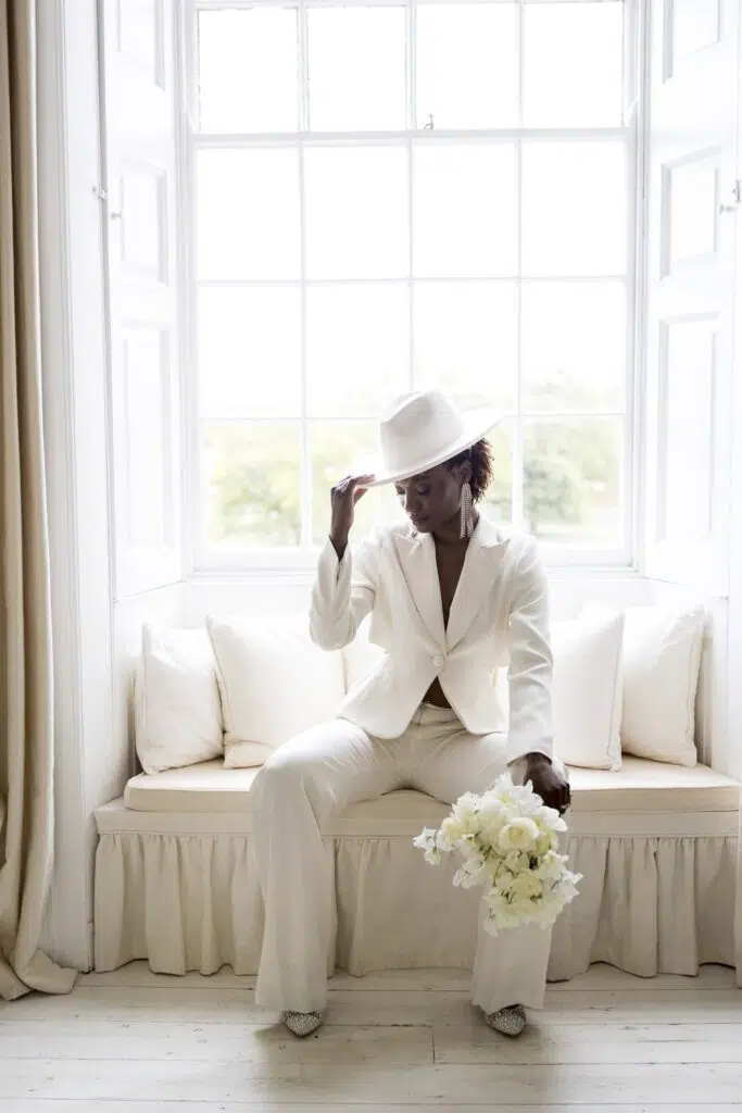 a bride in her wedding suit sitting o the window sill in the bedroom of butley priory