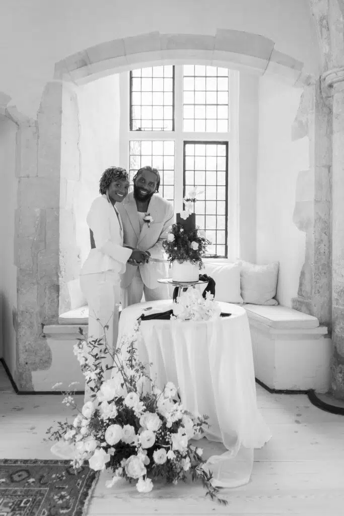 black and white image of bride and groom cutting a wedding cake at butley priory