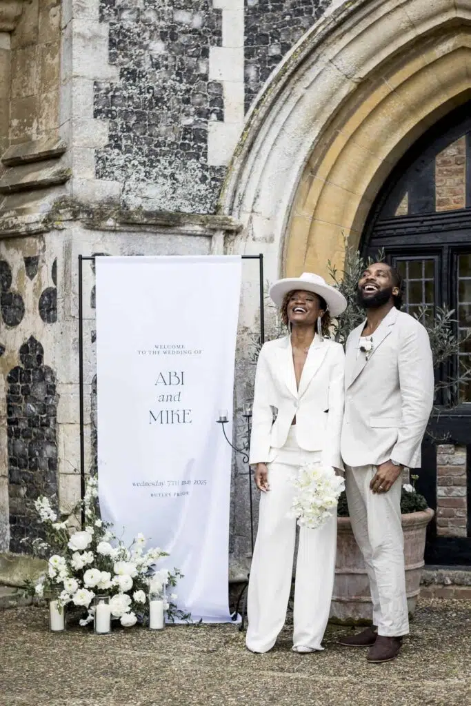 a couple laughing outside at butler priory in front of their wedding banner