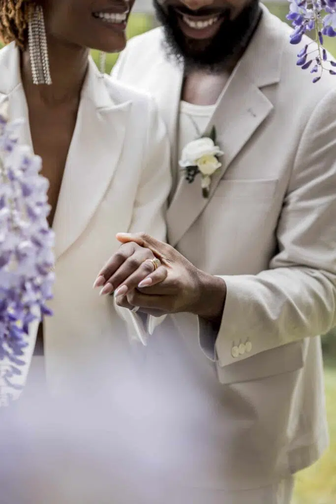a bride and groom holding hands to show off their wedding rings under the wisteria at butlley priory