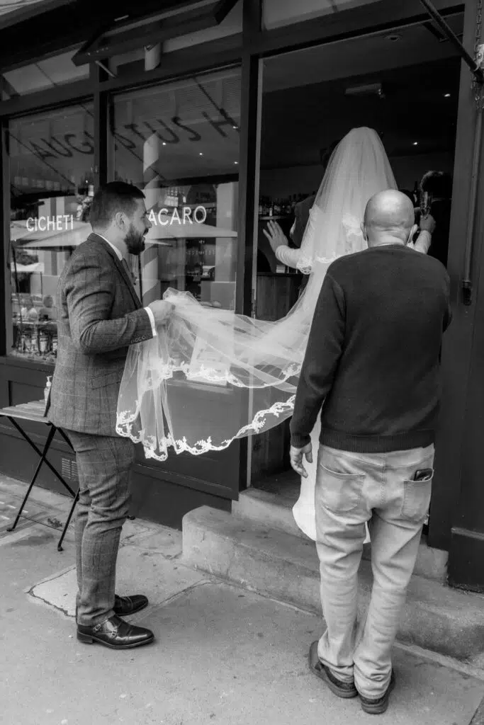 A groom holds the bride's veil as she enters her wedding reception