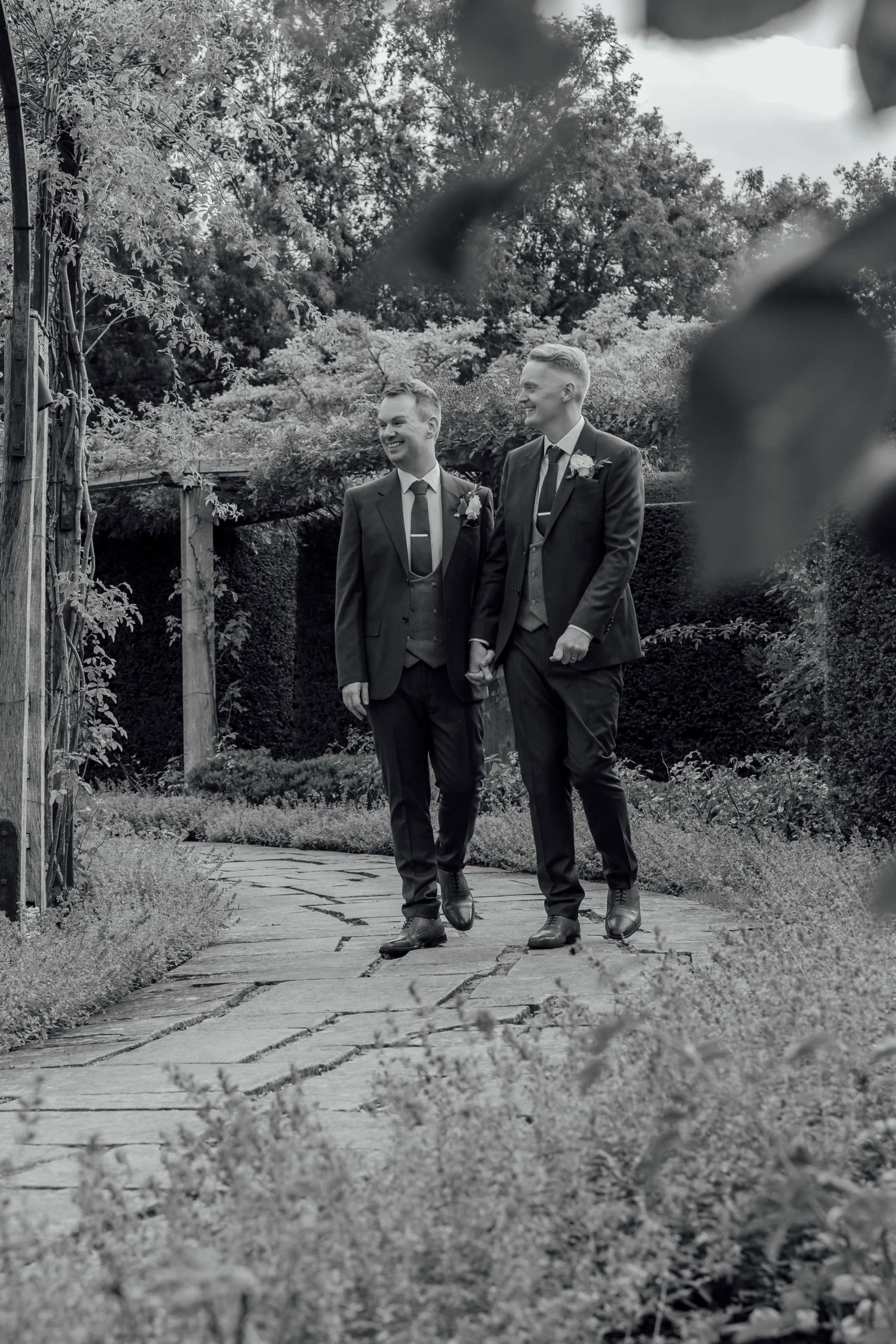 Two grooms walk through the gardens at Great Fosters. Photographed by LGBTQ wedding photographer Ross Willsher