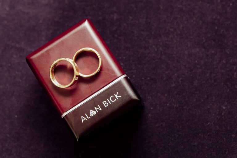 A close up of the couple's wedding rings on top of their Alan Rick box on a purple cushion