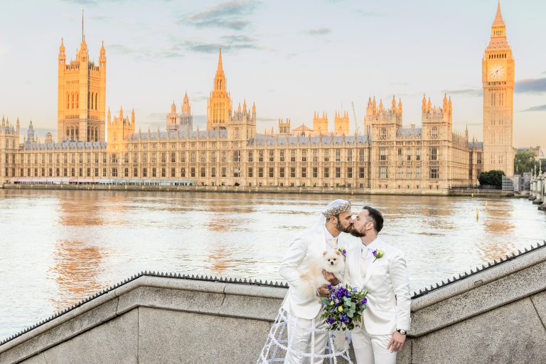 Pete and Will kissing with the Thames and the Houses of Parliament behind them.