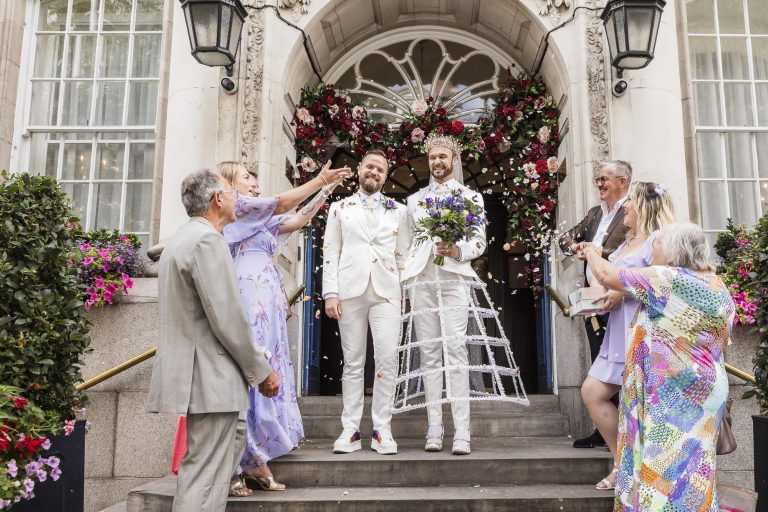 Family and friends throwing confetti over Pete and Will on the steps of Chelsea Old Town Hall after their intimate LGBTQ+ micro wedding ceremony.