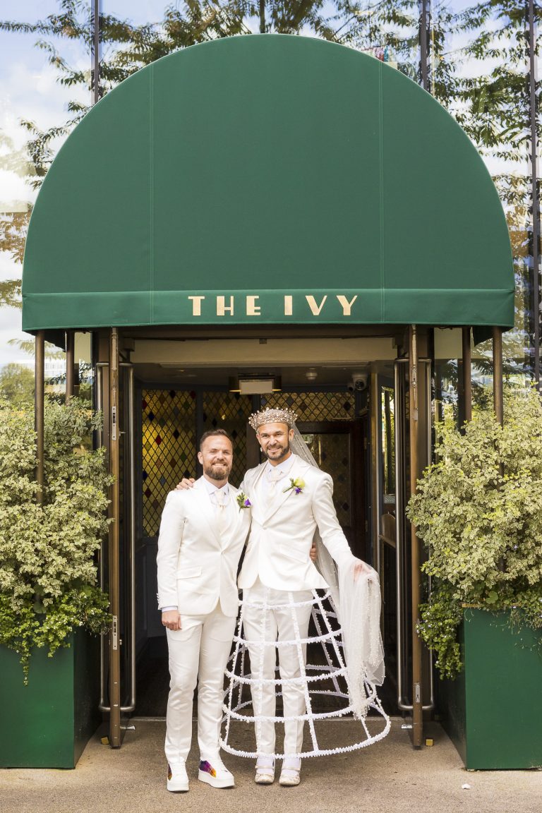 Pete and Will beneath the green awning of The Ivy restaurant in London, celebrating after their Chelsea Old Town Hall micro wedding.