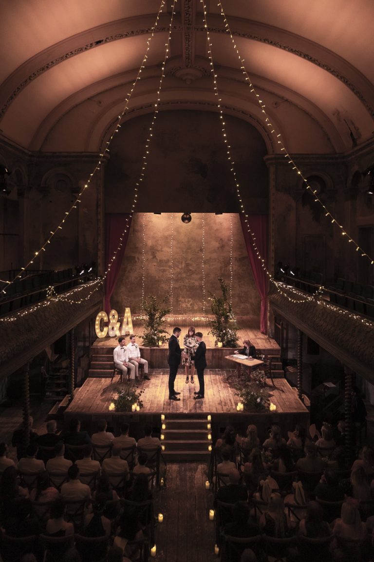 LGBTQ+ couple exchanging wedding vows on the stage at Wilton's Music Hall in London. A natural, unstaged moment during their London wedding, photographed with a gentle, storytelling approach